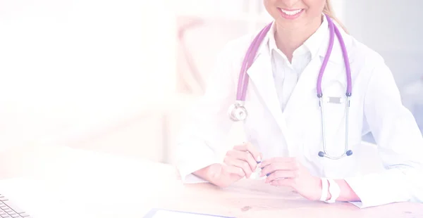 Bonito jovem sorridente médico feminino sentado na mesa e escrevendo. — Fotografia de Stock