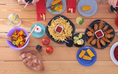 Ahşap masada otururken birlikte yemek yiyen bir grup insanın üst düzey görüntüsü. Masada yemek var. İnsanlar fast food yiyor..