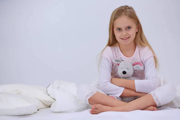 Little girl in the bedroom is sitting on the bed. Little girl is wearing a pajamas and sitting in bed .