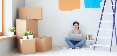 Yeni daire dizüstü bilgisayar ile oturup, boyama sırasında genç kadın portre. Dizüstü bilgisayar ile genç kadın