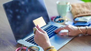 Kredi kartı tutan ve dizüstü bilgisayar kullanan genç bir kadın. Çevrimiçi alışveriş kavramı