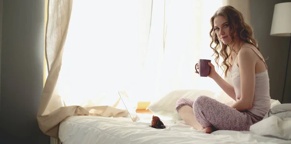 Jovem bela mulher sentada na cama com laptop . — Fotografia de Stock