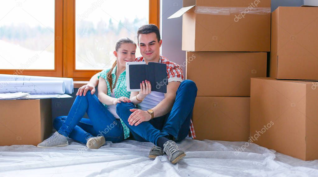 Couple moving in house sitting on the floor with ipad. Couple