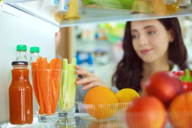 Sağlıklı yiyecek, sebze ve meyvelerle dolu açık buzdolabının yanında duran kadın portresi. Kadın portresi