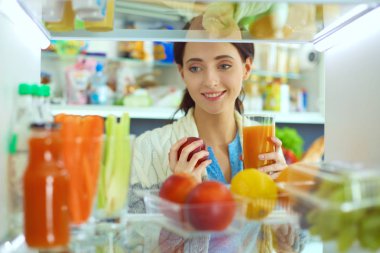 Sağlıklı yiyecek, sebze ve meyvelerle dolu açık buzdolabının yanında duran kadın portresi. Kadın portresi