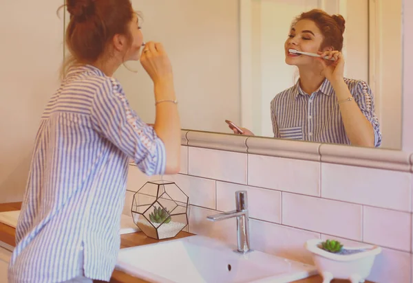 Mladá krásná žena čištění zubů před zrcadlem — Stock fotografie