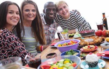 Ahşap masada otururken birlikte yemek yiyen bir grup insanın üst düzey görüntüsü. Masada yemek var. İnsanlar fast food yiyor..