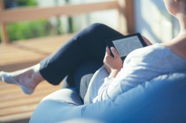 Touchpad ile kanepede oturan gülümseyen genç kadın.