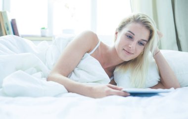 Elinde boş ekranlı dijital tablet tutan ve yatak odasında kameraya gülümseyen bir kız.