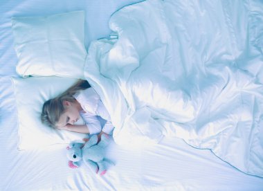 çocuk oyuncak oyuncak ayı ile yatakta uyur küçük kız.