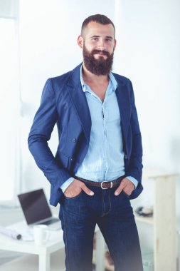 Ofiste duran mutlu iş adamı, arka planda masa başında çalışan iş arkadaşları.