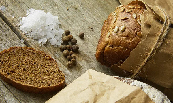 Dva bochníky chleba zabalené v papíru na dřevěném stole se solí a papírkem. Oříznutá fotografie — Stock fotografie