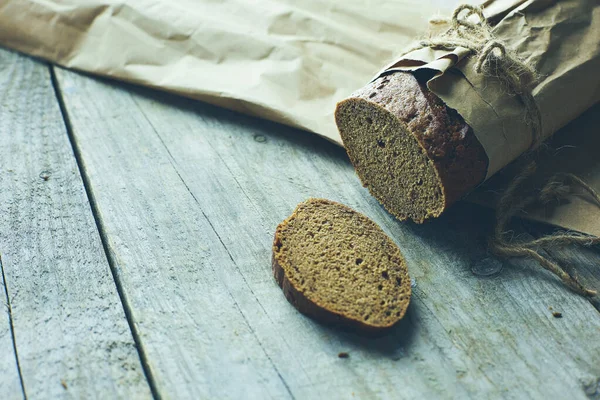 Brood in plakjes, verpakt in papier op houten tafel — Stockfoto