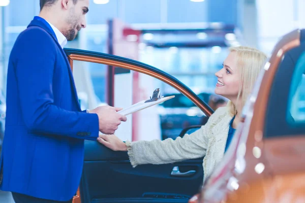 美しい若い女性が話しているハンサムな車販売店労働者のディーラーで車を選んでいる間 — ストック写真