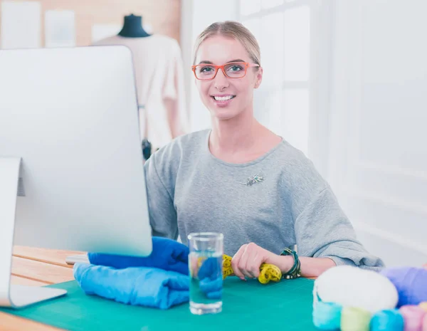 Um retrato de uma jovem designer usando um laptop e sorrindo, roupas penduradas como fundo — Fotografia de Stock
