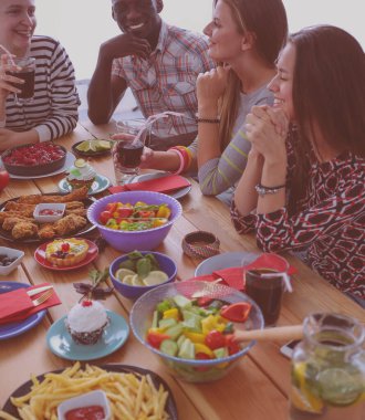 Ahşap masada otururken birlikte yemek yiyen bir grup insanın üst düzey görüntüsü. Masada yemek var. İnsanlar fast food yiyor..
