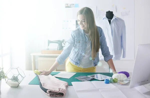Krásná módní návrhářka stojící u stolu ve studiu — Stock fotografie