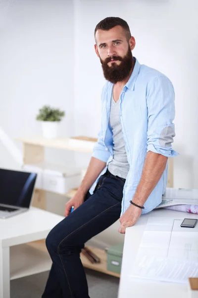 Retrato de un joven diseñador sonriente apoyado en una mesa de ordenador mientras está solo en una oficina moderna —  Fotos de Stock