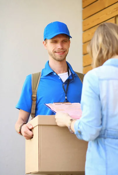 Repartidor sonriente con uniforme azul que entrega la caja de paquetes al destinatario: concepto de servicio de mensajería. Repartidor sonriente en uniforme azul —  Fotos de Stock