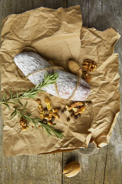 Italian salami wih sea salt, rosemary, garlic and nuts on paper. Rustic style. Top view. — Stock Photo, Image