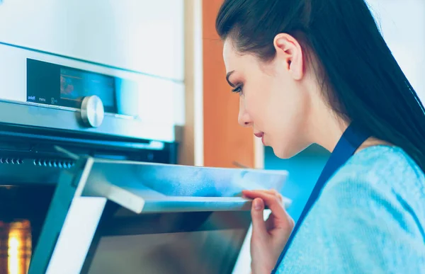 Hermosa joven comprobando cómo le va a su pastel en el horno — Foto de Stock