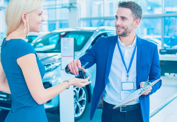Car salesman sells a car to happy customer in car dealership and hands over the keys
