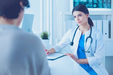 Doktor ve hasta hastane danışma odasında tıbbi sorunları tartışıyorlar. Doktor hasta formunu dolduruyor.