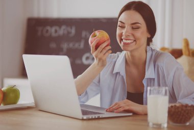 Elma ve dizüstü bilgisayar mutfakta oturan kadın
