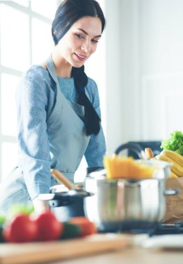 Sebzeli alışveriş poşeti taşıyan genç bir kadın. Mutfakta duruyor.