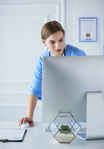 Portrait of female physician filling up medical form while standing near reception desk at clinic or emergency hospital