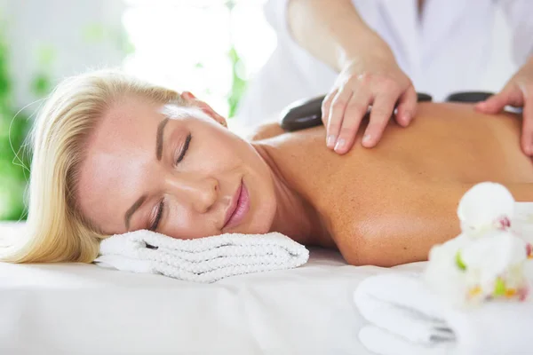 Vacker ung kvinna med ögonen stängda mottagande massage med varma stenar på salon spa — Stockfoto