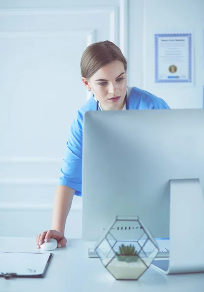 Portrait of female physician filling up medical form while standing near reception desk at clinic or emergency hospital