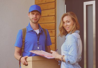 Mavi üniformalı gülümseyen kurye servis konseptine paket kutusu teslim eden teslimatçı. Mavi üniformalı gülümseyen teslimatçı.