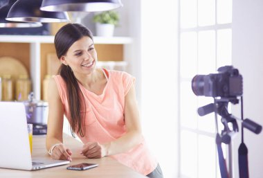 Mutfakta dizüstü bilgisayara benzeyen tariflerle gülümseyen genç bir kadın. Gıda blogcusu kavramı