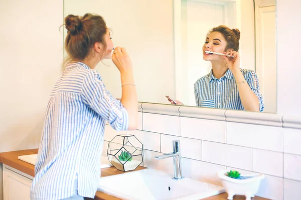 Jovem mulher bonita escovando os dentes na frente do espelho — Fotografia de Stock