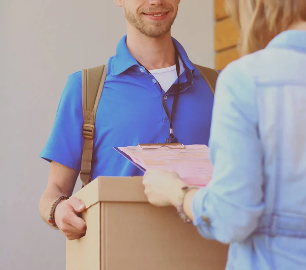 Repartidor sonriente con uniforme azul que entrega la caja de paquetes al destinatario: concepto de servicio de mensajería. Repartidor sonriente en uniforme azul — Foto de Stock