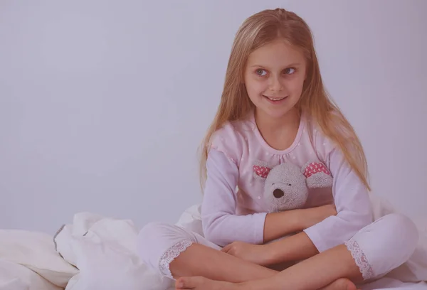 La niña en el dormitorio está sentada en la cama. La niña está usando un pijama y sentada en la cama  . —  Fotos de Stock