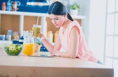 Mutfakta dijital tablet kullanan güzel genç bir kadın.