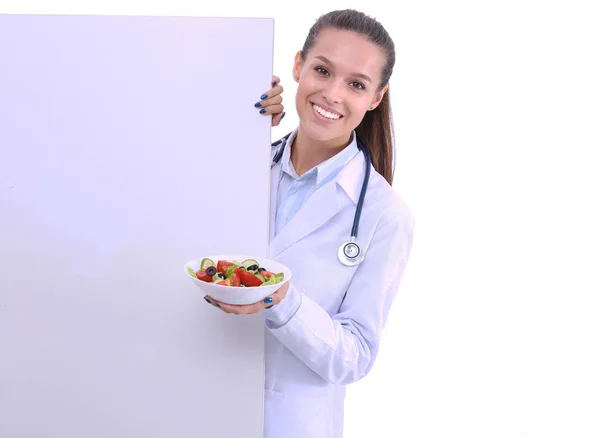 Πορτρέτο ενός όμορφου γιατρού γυναίκα κρατώντας ένα πιάτο με φρέσκα λαχανικά στέκεται κοντά στο κενό. Γυναίκες γιατροί — Φωτογραφία Αρχείου