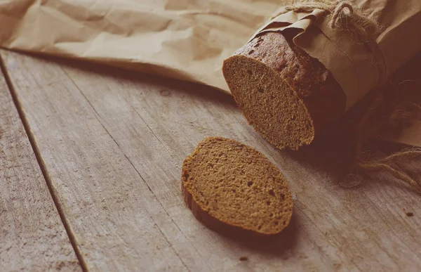 Brood in plakjes, verpakt in papier op houten tafel — Stockfoto