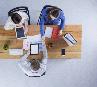 Genç iş adamları dizüstü bilgisayarlarını kullanarak masa başında birlikte çalışıyorlar.