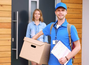 Mavi üniformalı gülümseyen kurye servis konseptine paket kutusu teslim eden teslimatçı. Mavi üniformalı gülümseyen teslimatçı.