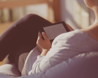 Touchpad ile kanepede oturan gülümseyen genç kadın.