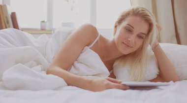 Elinde boş ekranlı dijital tablet tutan ve yatak odasında kameraya gülümseyen bir kız.