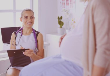 Steteskoplu ve tabletli genç kadın doktor hastanede hamile bir kadınla konuşuyor..
