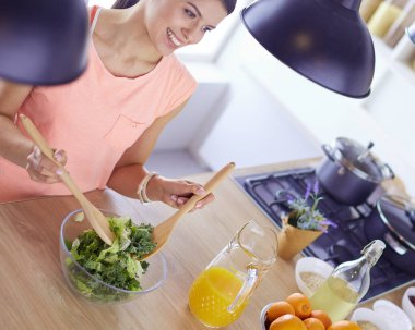 Gülümseyen genç kadın mutfakta taze salata karıştırıyor..