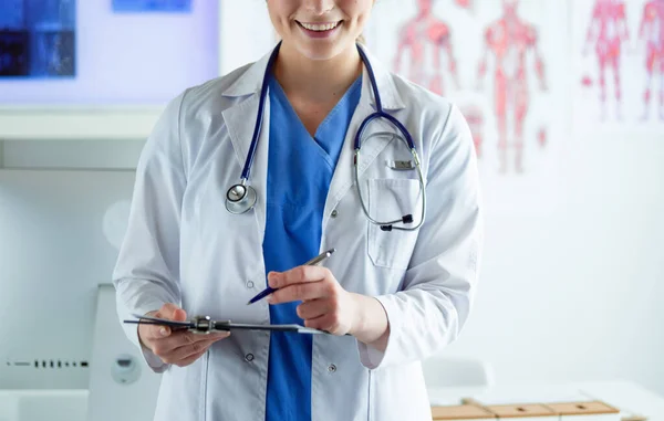 Dottore con uno stetoscopio, con un quaderno in mano. Primo piano di un medico di sesso femminile che compila il modulo medico negli appunti mentre si trova dritto in ospedale — Foto Stock