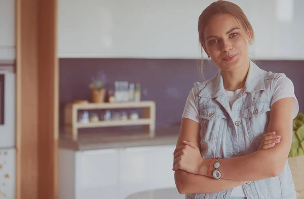 Portrait of young woman standing with arms crossed against kitchen background — Stock Photo, Image