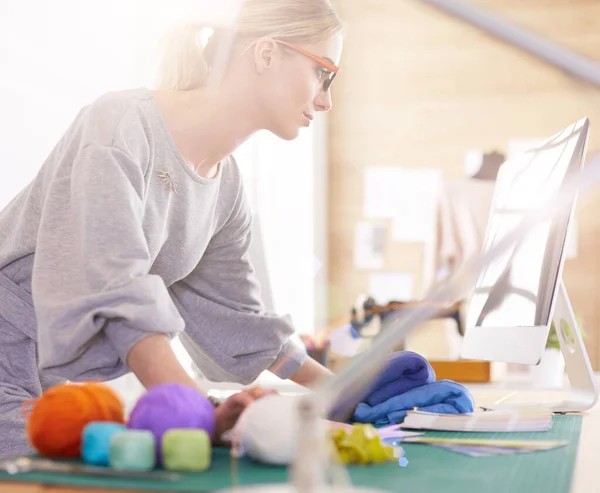 Een portret van een jonge Aziatische ontwerper vrouw met behulp van een laptop en glimlachend, kleren opgehangen als achtergrond — Stockfoto