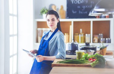 Mutfakta yemek yapmak için tablet bilgisayar kullanan genç bir kadın.